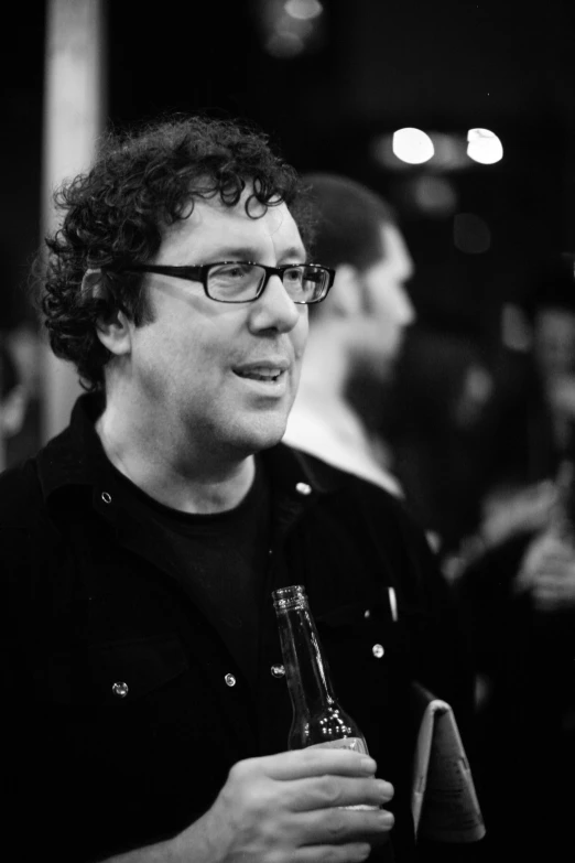 a man with curly hair wearing glasses holding a beer