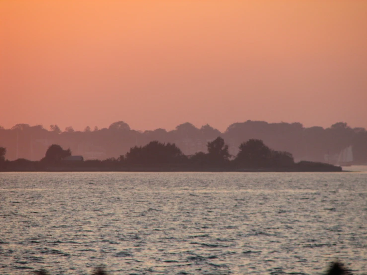 a distant tree lined area on a lake at sunset