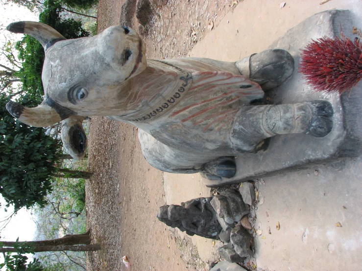 a statue of a cow in front of rocks and some bushes