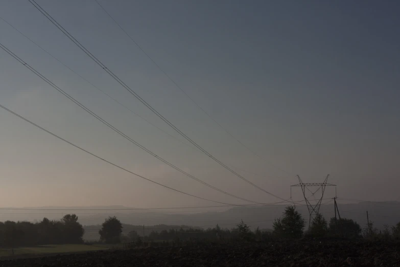 telephone wires at dusk over some trees in the hills