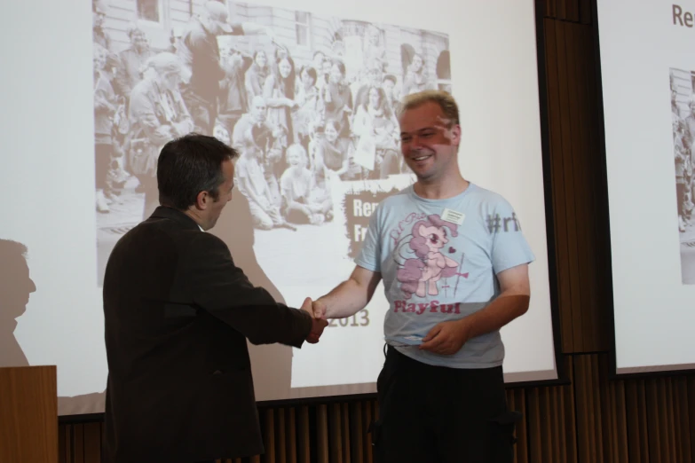 two men shake hands near one another on a stage