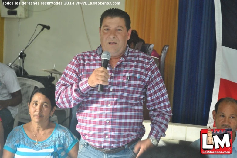 a man in a checkered shirt with his microphone up to his chest