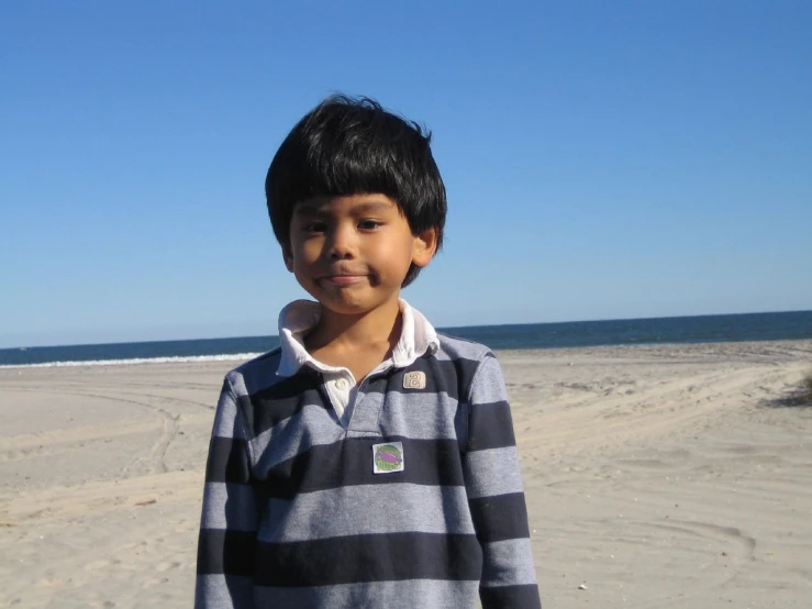 a little boy standing on the beach looking at the camera