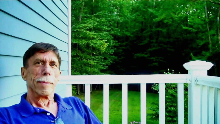 an elderly man is sitting on his porch and looks off into the distance