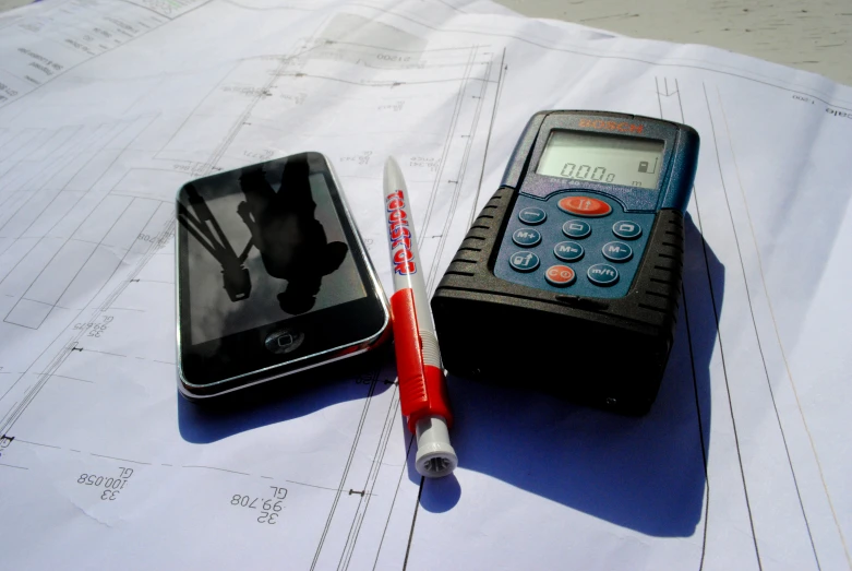 a pen, calculator and smartphone on some construction documents