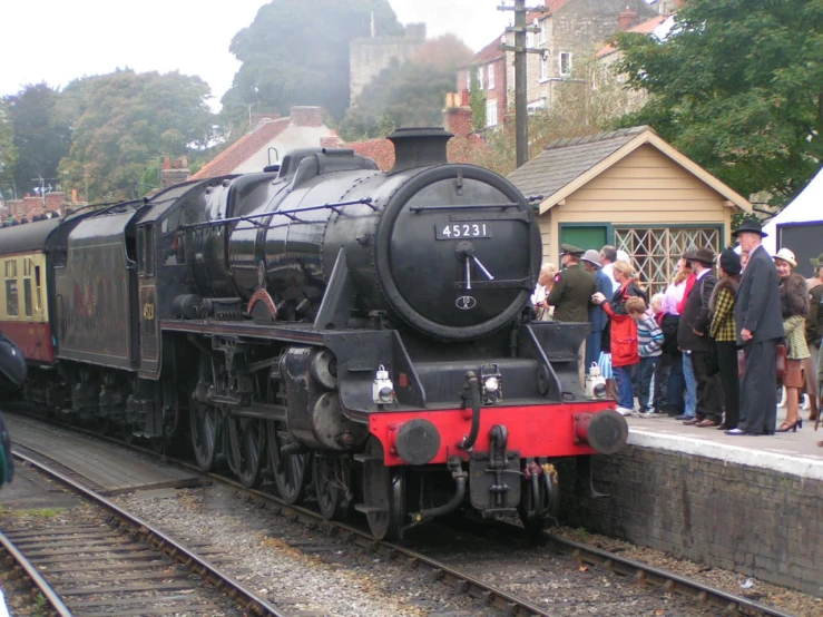 people are gathered around the old fashioned train on the tracks