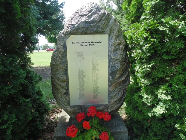 a large stone sign sits in the grass near bushes