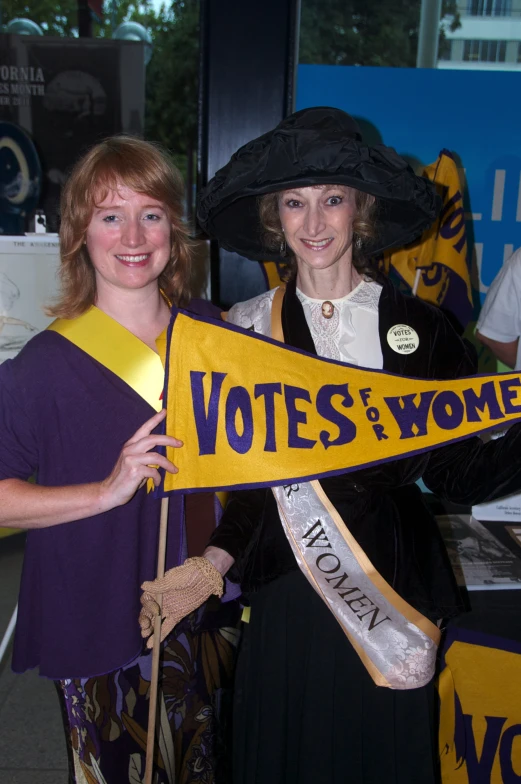 two woman holding a political sash that reads vote f'women