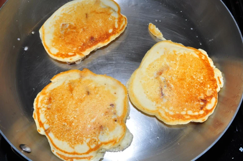 three pancakes in a pan with syrup are cooked