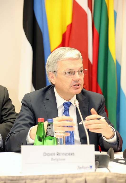 a man in suit sitting at a table in front of some flags