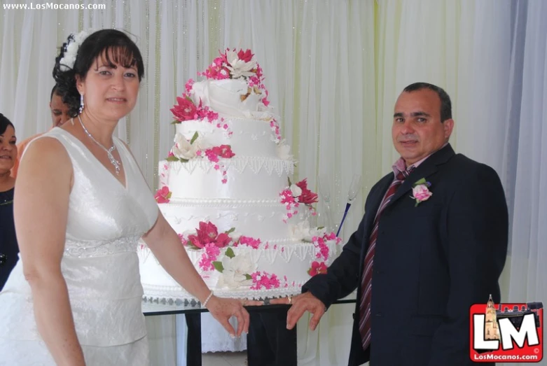 a bride and groom stand next to a three layer white cake