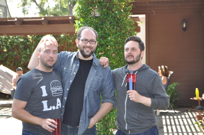 three men are standing by the house holding red item