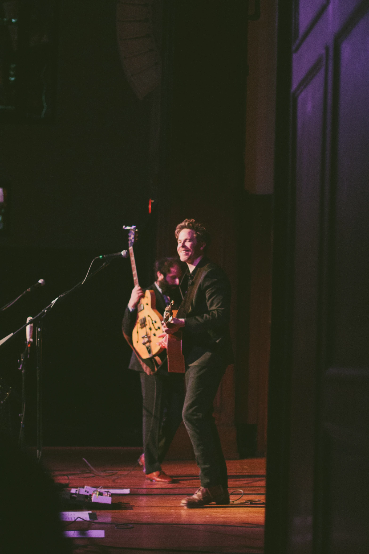 two young men perform at a stage, one playing the guitar