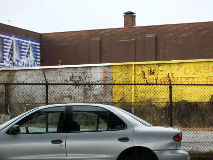 a small silver car parked by a fence