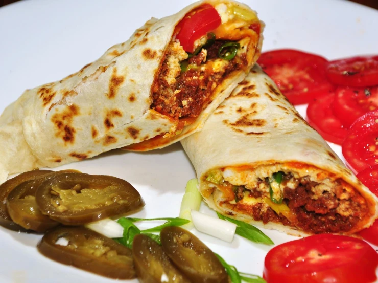 a burrito is on a plate with tomatoes, pepperonis and sliced peppers