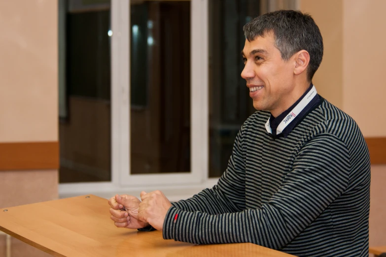 a man sitting at a table smiling and looking to his right