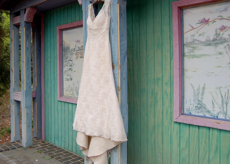 a lace wedding dress hangs out the front door of a wooden shack