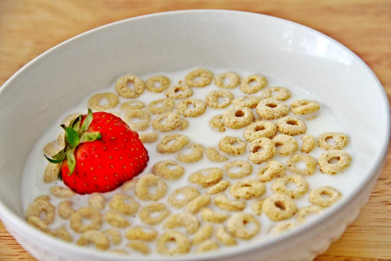 a white bowl with cereal and a strawberry in it