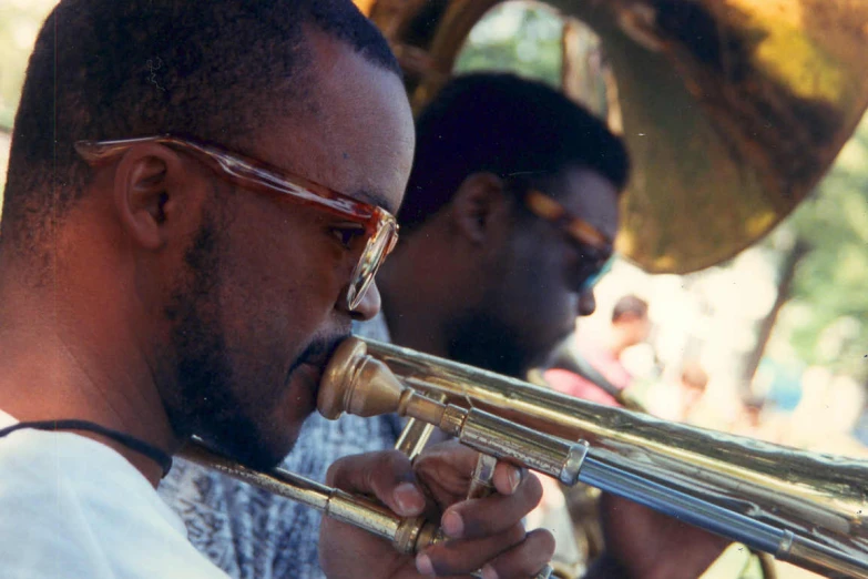 a man in sunglasses playing the trombone and another man in glasses