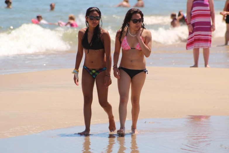 two women are walking on the beach with the ocean in the background