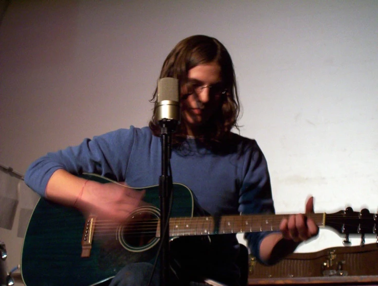 man playing guitar while singing into microphone in home studio