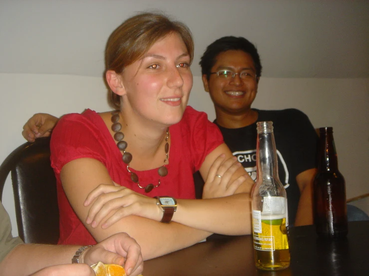 a man and woman smiling as they sit at a table with a beer