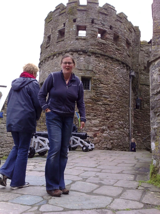 two women are standing on the brick sidewalk outside of an old castle