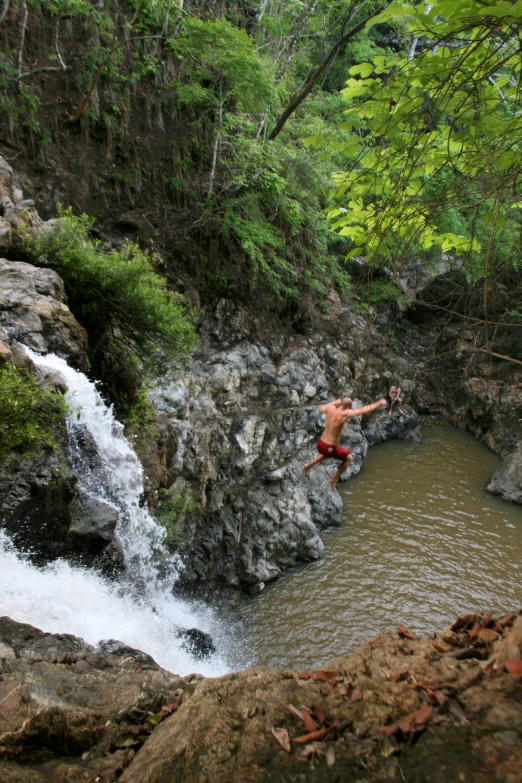 a man jumping off of a waterfall into a river