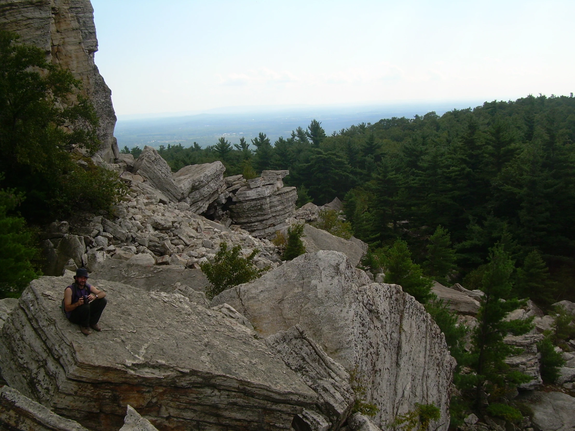 a woman is sitting on a rocky outcropping, and looks over the landscape