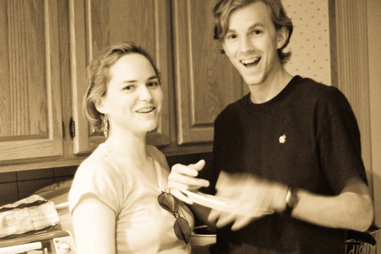 a man and woman standing in a kitchen, one is holding a plate