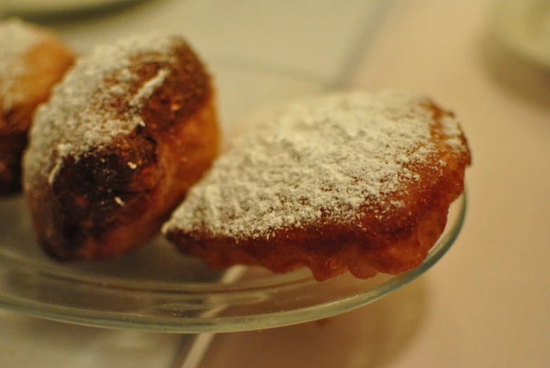 two powdered sugar donuts are on a glass cake plate