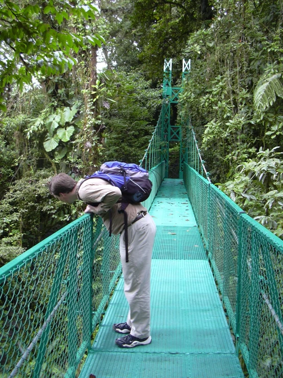 a man in grey pants and backpack standing on a rope bridge