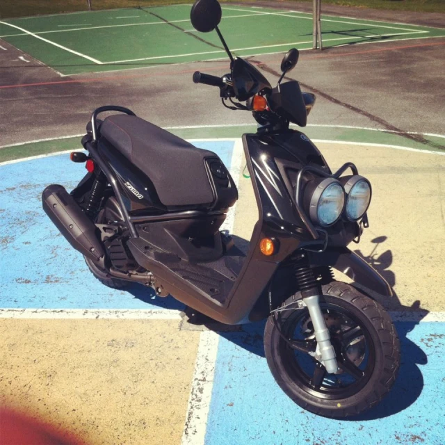 a scooter parked on the parking lot of a tennis court