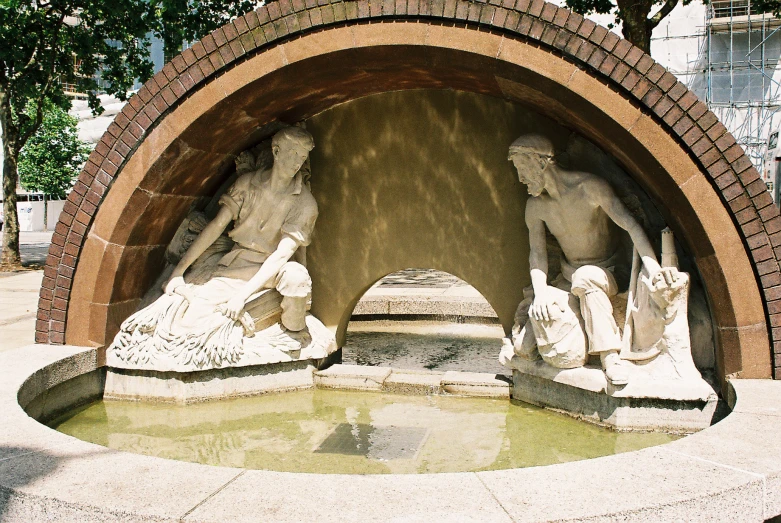 some statues in front of an arch above a pond