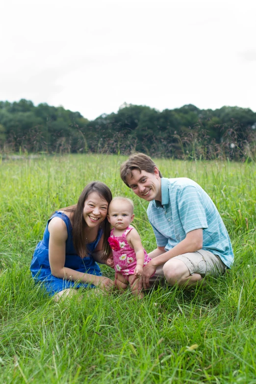 a man and woman kneeling down with their child on a grassy field