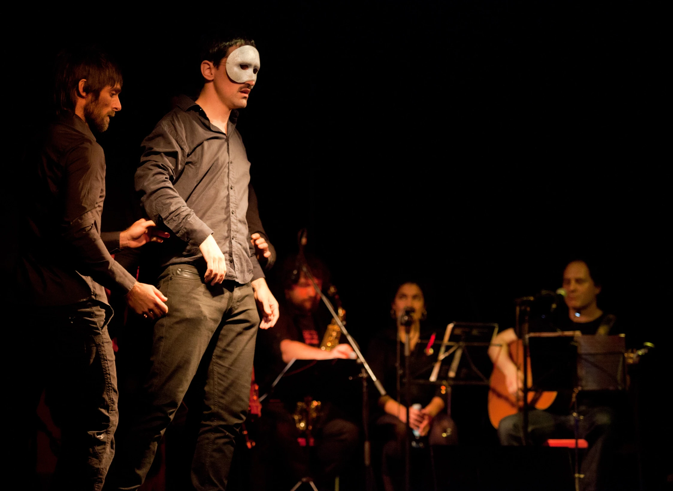 several people stand at a stage while one person wearing an masks