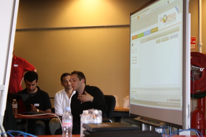 men sitting at a table in front of a projector screen