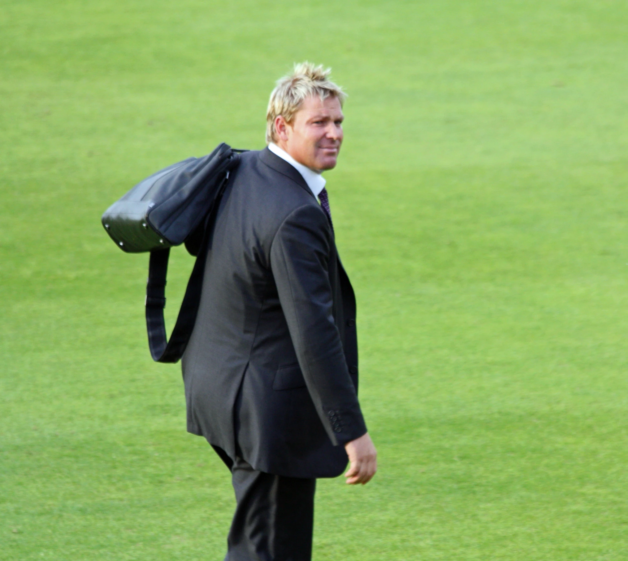 a man in black suit carrying a bag walking on green grass
