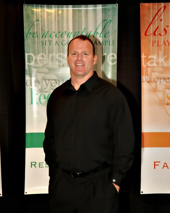 a man standing next to some banners and smiling