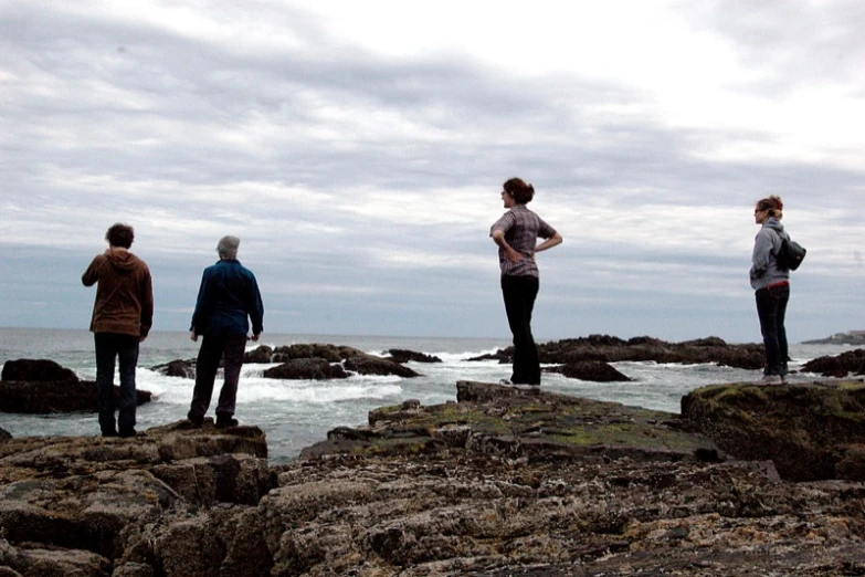 the people are standing on the rocks at the ocean