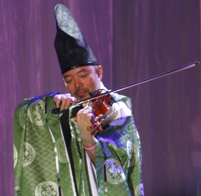 an oriental musician plays his violin in front of purple curtain