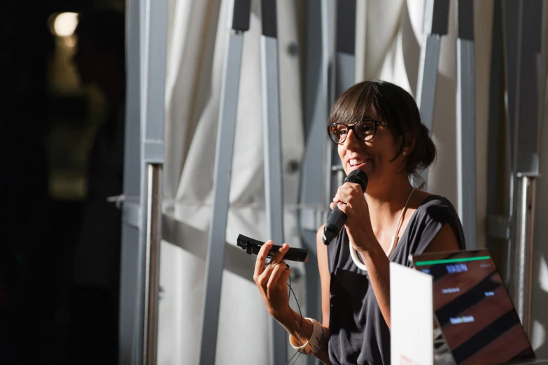 a woman wearing glasses talking into a microphone