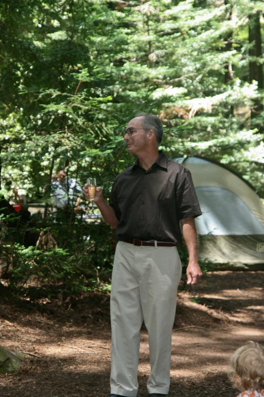 man in glasses holding out a beverage by tent