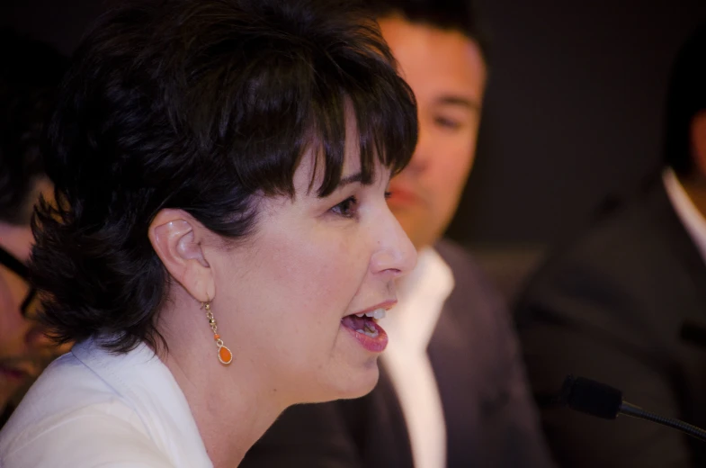 a woman wearing ear rings speaking at a microphone