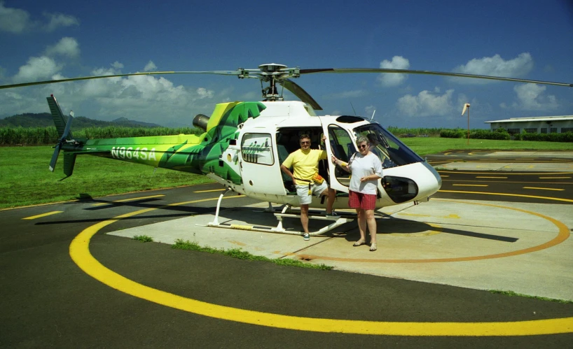 two people standing next to a helicopter parked on a runway
