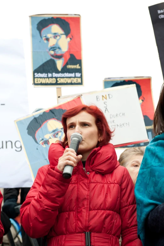 a woman speaks into a microphone while surrounded by protesters