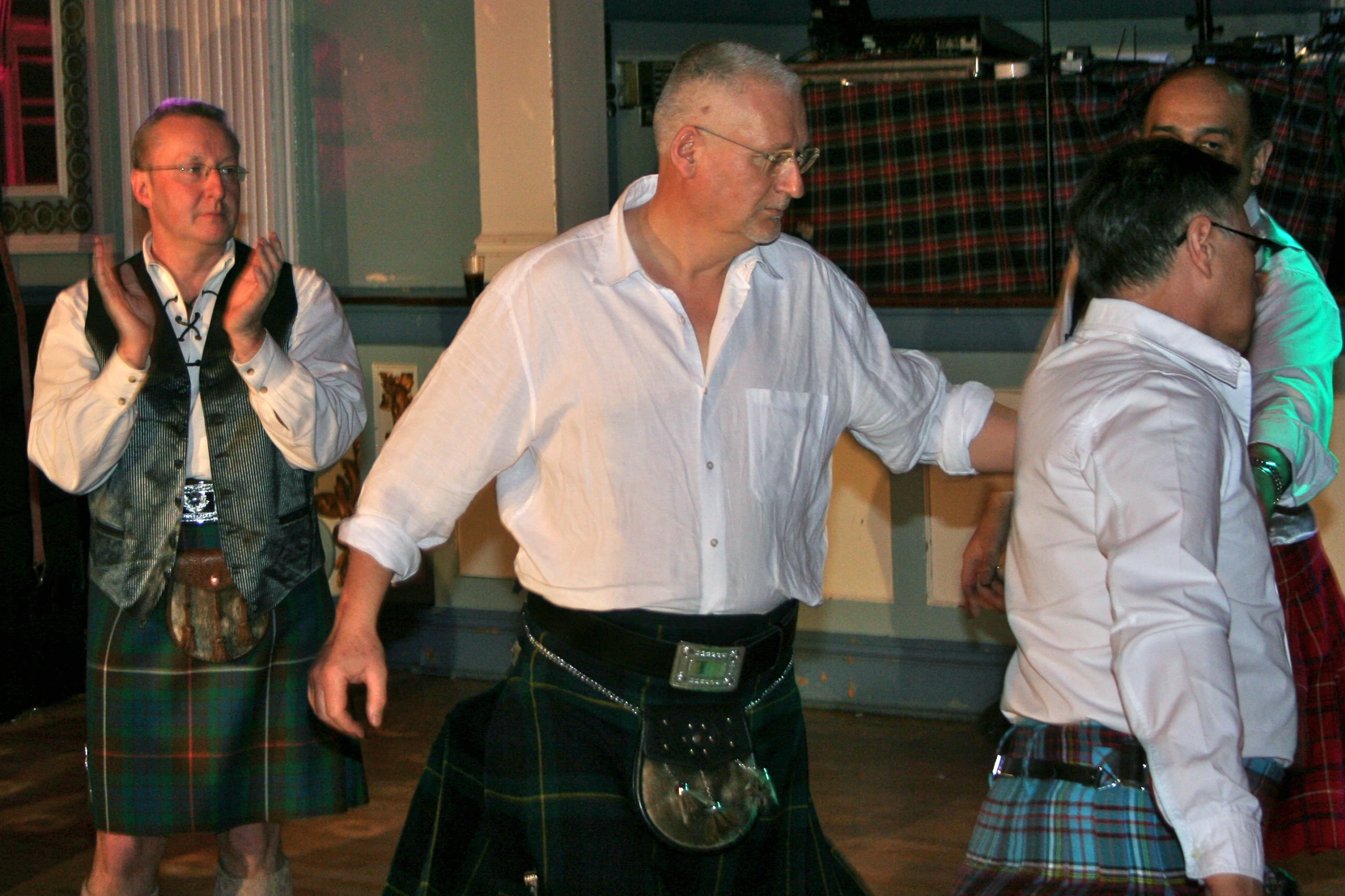 man in kilts at party dancing with two men standing behind him