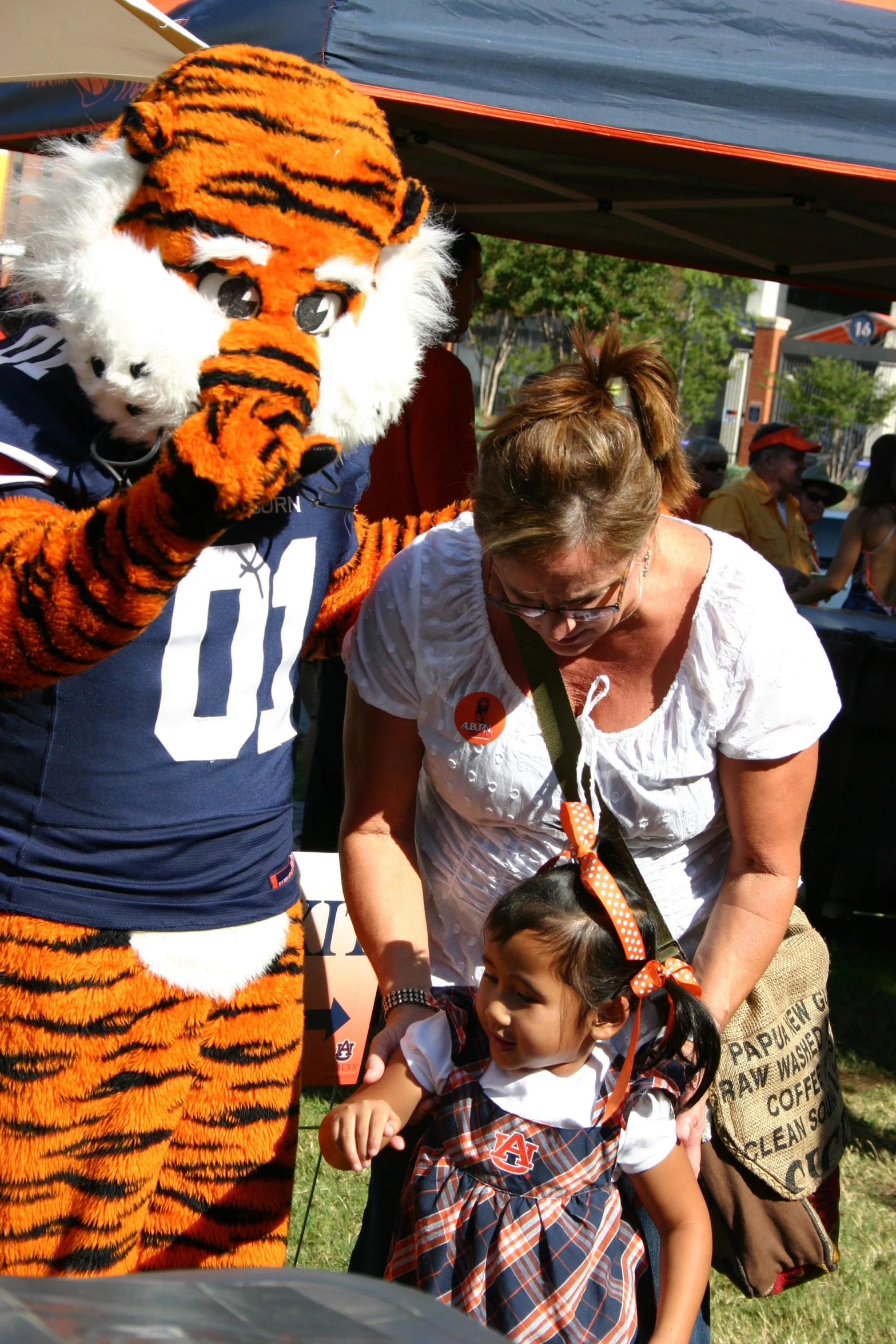 a woman and young child standing in front of a large tiger mascot