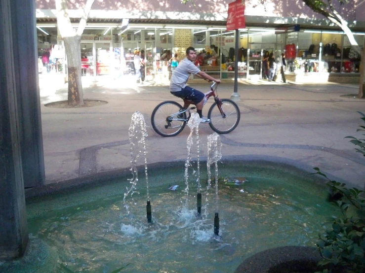 man balancing on bicycle in fountain near storefront