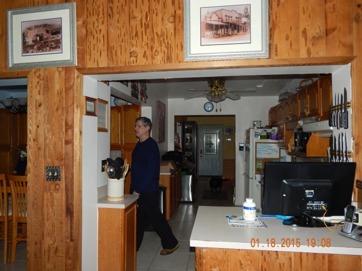 man with eye glasses walking through a kitchen with wooden paneling